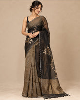 A woman modeling a black and gold saree with floral embroidery and a pleated pattern, set against a solid beige studio background.