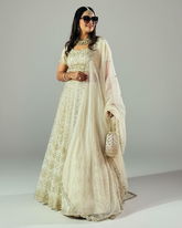Woman wearing a white embroidered lehenga with a plain background
