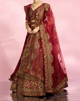 Woman wearing a traditional maroon and gold embroidered outfit on a pink background