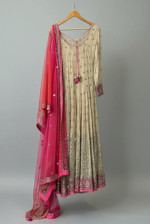Traditional outfit with a pink dupatta hanging on a hanger in a room.