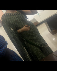 A person wearing a dark green saree with a subtle gold pattern and a silver embroidered neckline, shown in a mirror selfie in an indoor setting.