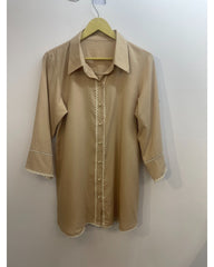 A beige long-sleeve button-up shirt with delicate white lace trim along the front placket, cuffs, and hem, hanging on a wooden hanger against a plain wall.