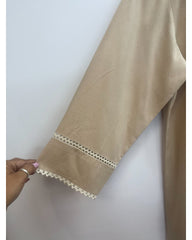A close-up of a beige garment sleeve with a decorative cream-colored crochet lace trim at the cuff, held by a hand against a plain light background.