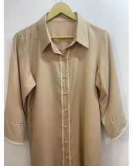 A beige long-sleeve button-up shirt with decorative white lace trim along the front placket and cuffs, hanging on a wooden hanger against a plain light background.