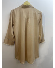 A beige long-sleeve tunic shirt with decorative eyelet trim on the cuffs and a scalloped edge along the hem, hanging on a wooden hanger against a plain light gray wall.