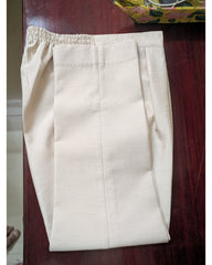 A pair of light beige trousers with an elastic waistband, folded and laid flat on a dark reddish-brown wooden surface.