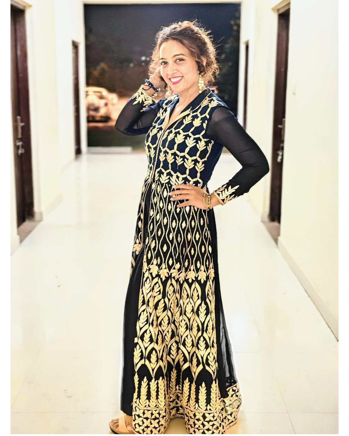 Woman wearing a black and gold patterned dress indoors.