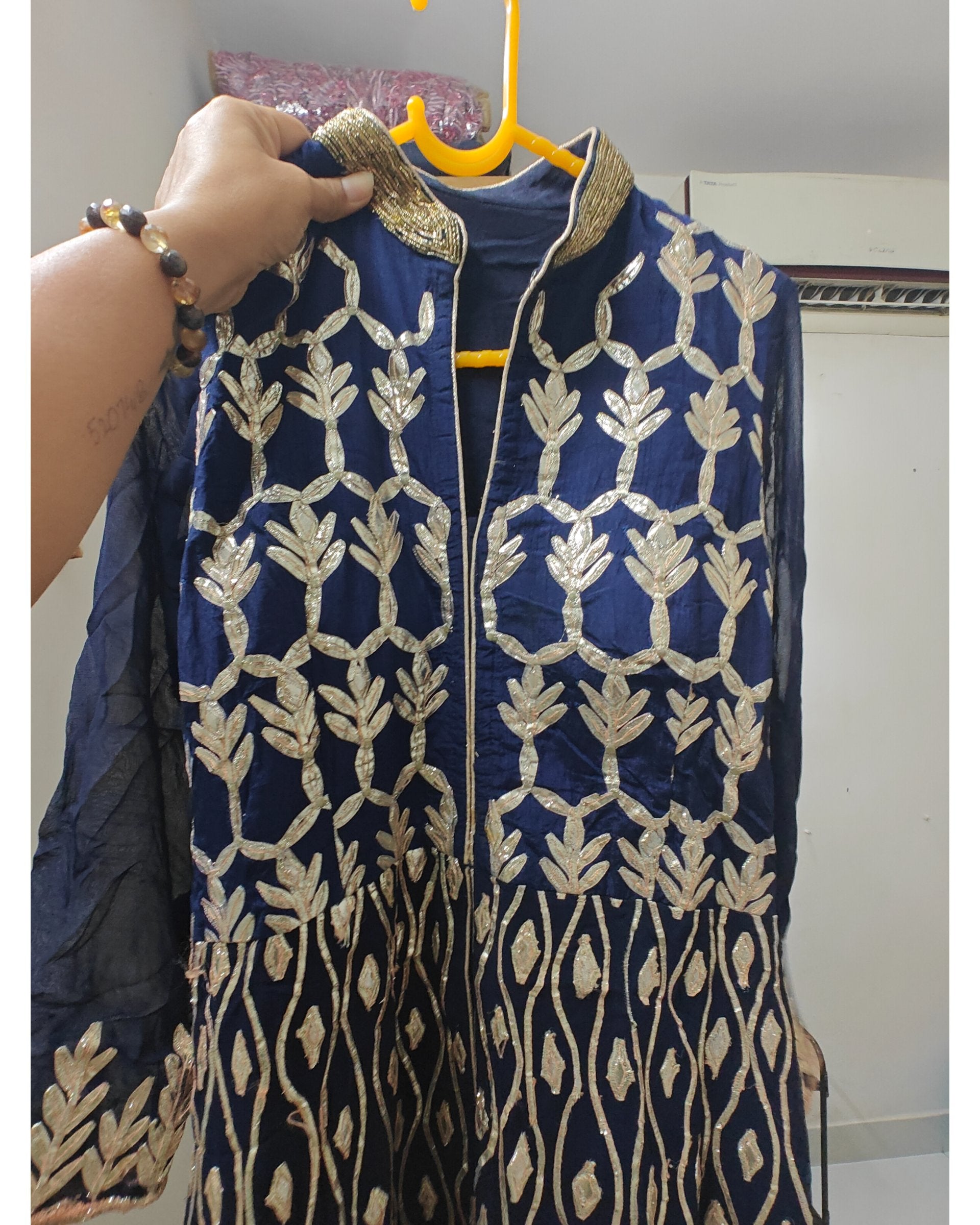 Navy blue embroidered jacket with gold patterns on a hanger.