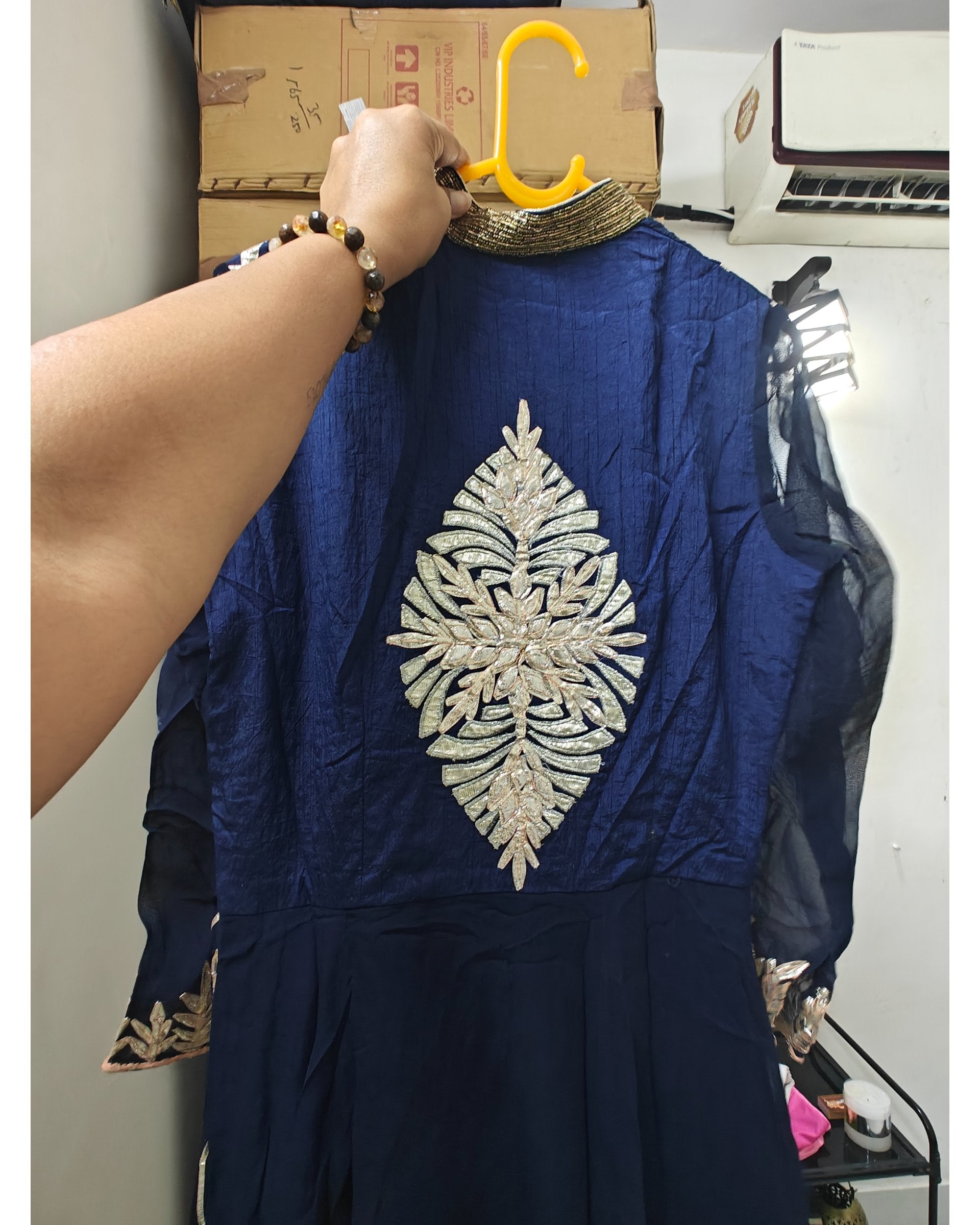 Navy blue dress with silver leaf embroidery held by a hand on a yellow hanger.