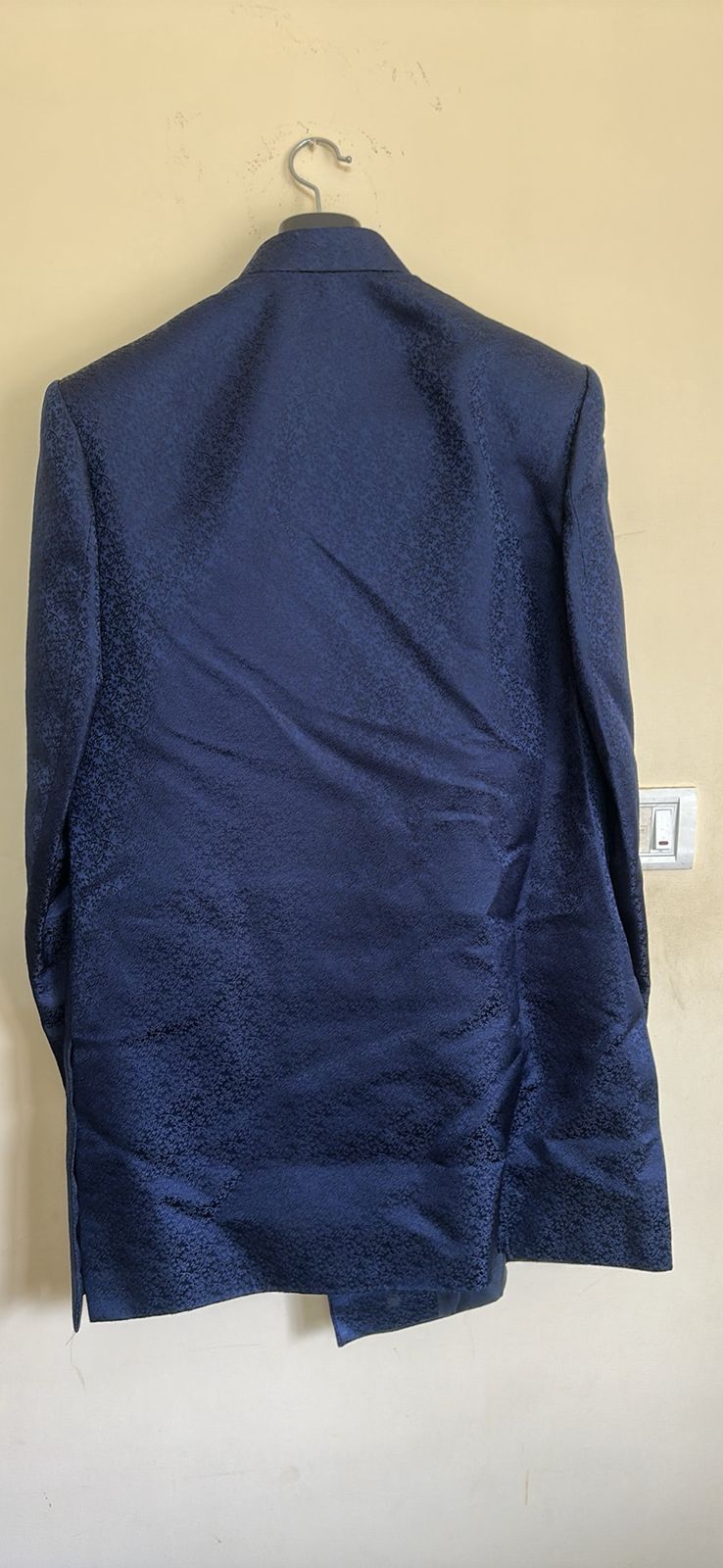 the back view of a Navy blue sherwani on a hanger against a beige wall.
