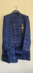 Blue sherwani jacket with gold buttons and embroidery on a beige wall.