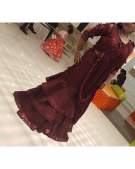 A woman wearing a deep maroon lehenga with sequined ruffles and a matching embellished blouse, standing in a dance hall with other dancers visible in the background.
