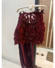 A deep burgundy lace and mesh dress with 3D floral appliques and gold embroidered details, hanging on a white plastic hanger in an indoor room.