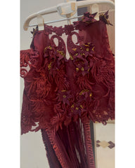 A close-up of a burgundy lace dress or costume top hanging on a white plastic hanger, featuring intricate floral applique and sheer mesh details.