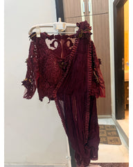 A deep maroon/burgundy embroidered ethnic outfit with a heavily embellished lace bodice, sheer draped sleeves, and matching draped fabric, hanging on a white hanger against an indoor wall.