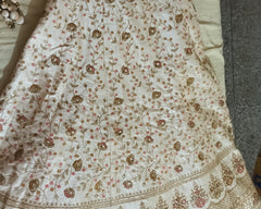 An embroidered cream-colored le, featuring intricate floral patterns in gold, pink, and brown thread, laid out on a neutral surface.