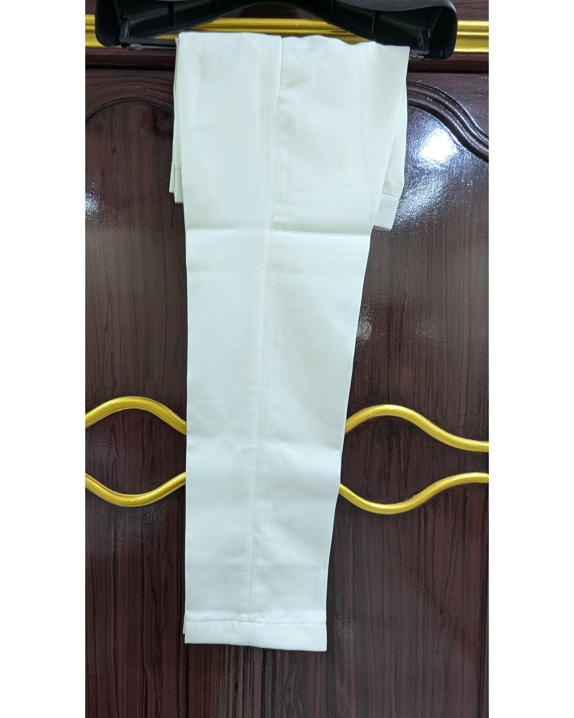 A pair of white trousers folded and hanging on a black hanger against a dark brown wooden door with gold-colored handles.