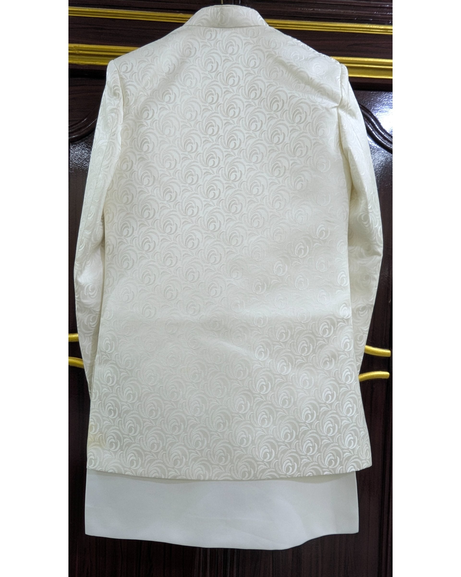 An off-white/cream traditional Indian jacket (kurta) with a subtle tonal floral jacquard pattern, shown hanging against a dark wood background.