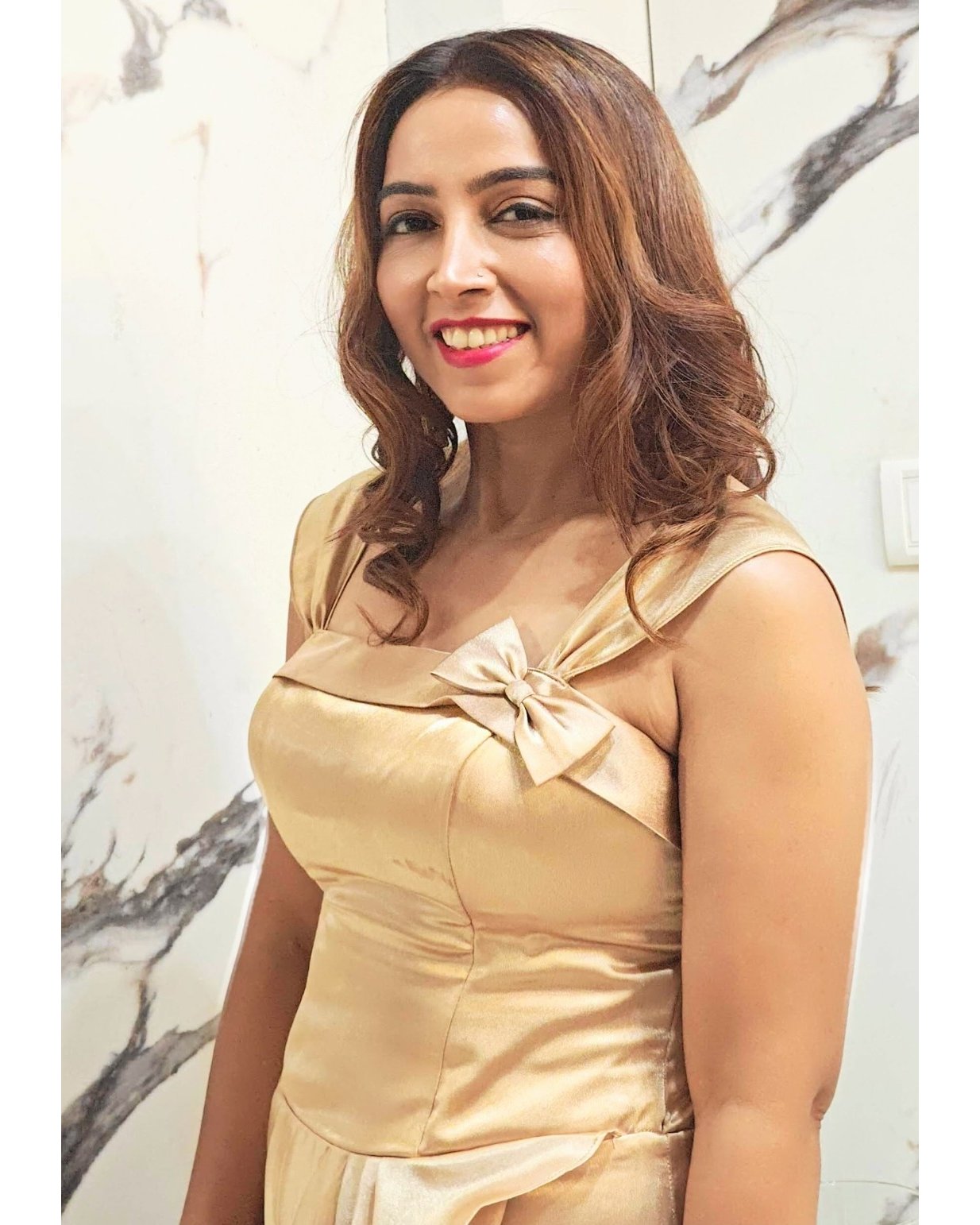 Woman wearing a beige dress with a bow detail against a marble wall.