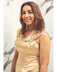 Woman wearing a beige dress with a bow detail against a marble wall.