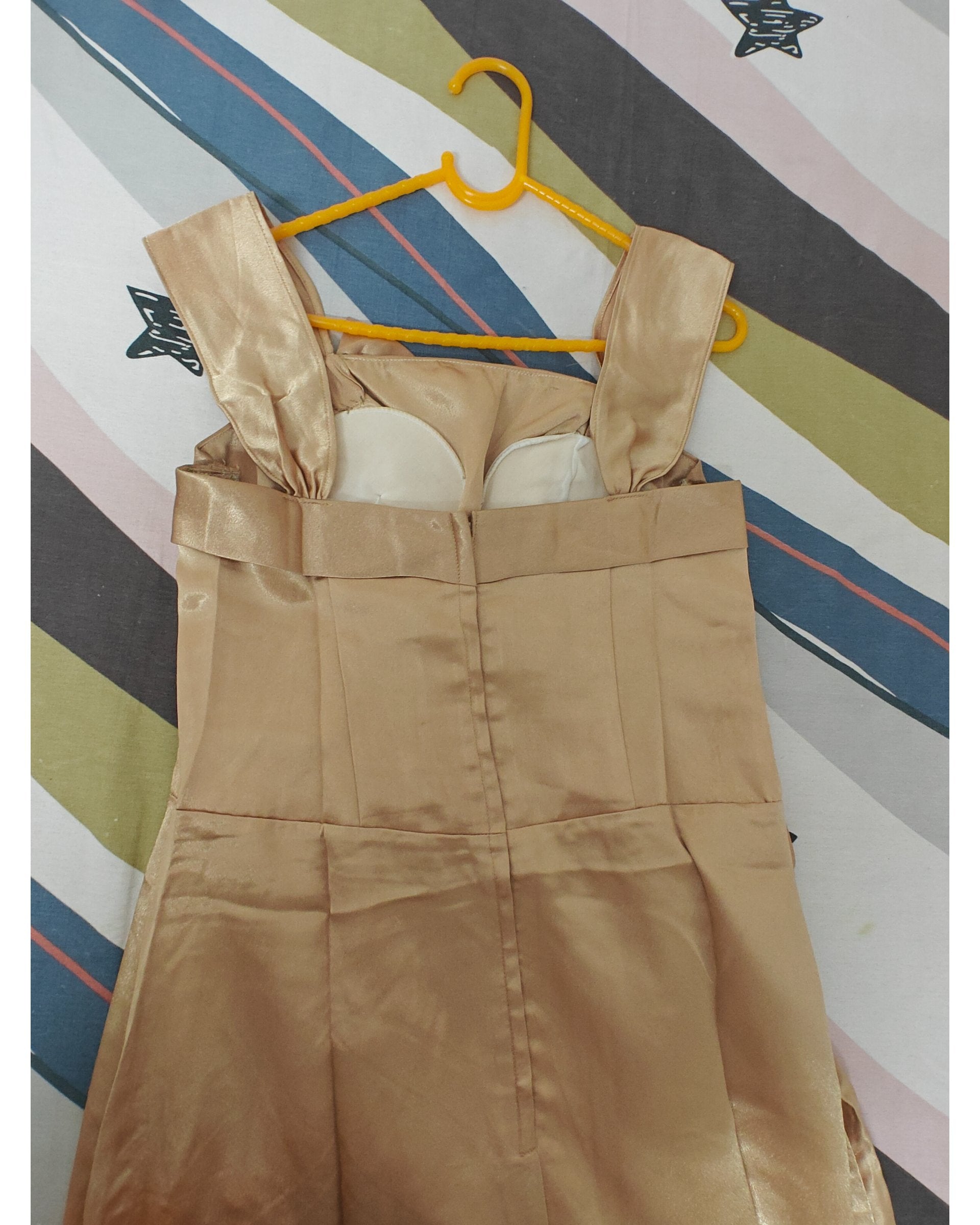 Beige gown on a yellow hanger against a striped background, back view