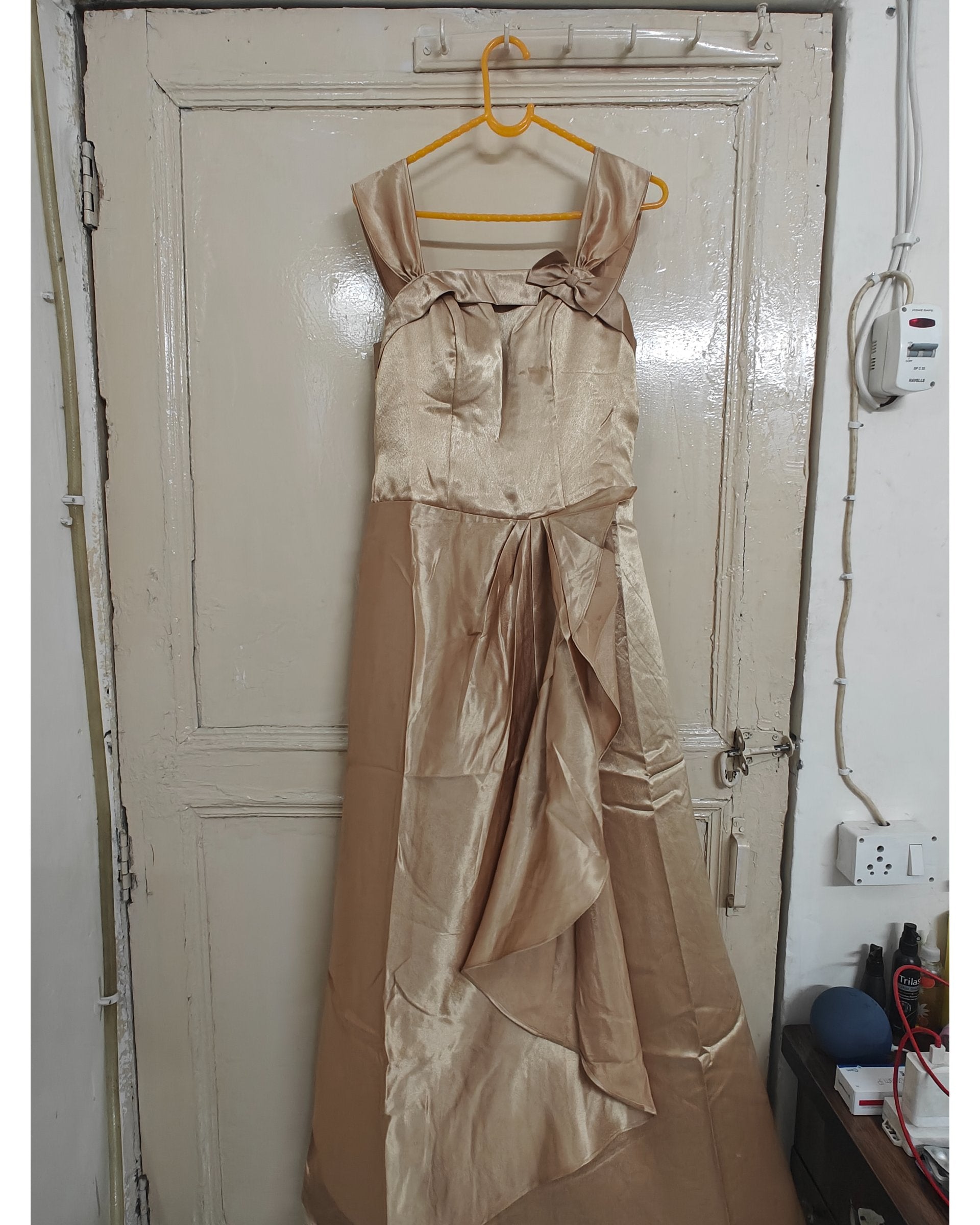Beige satin dress hanging on a yellow hanger against a white door.