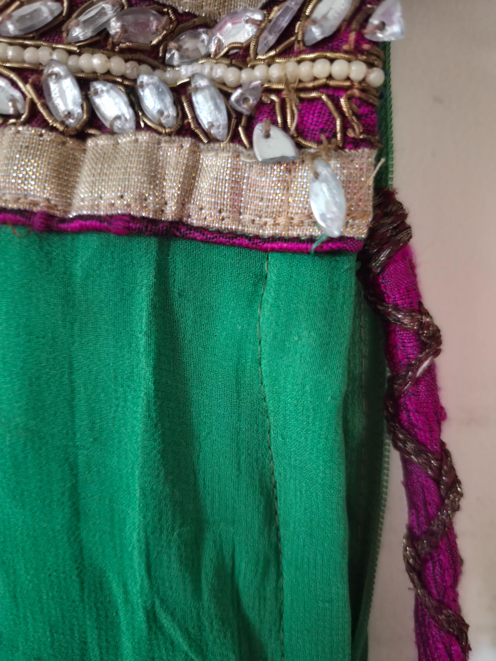 Close-up of a green lehenga with decorative gold and purple trim on a plain background showing slightly broken beads.