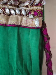 Close-up of a green lehenga with decorative gold and purple trim on a plain background showing slightly broken beads.