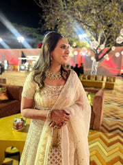 Woman in ivory lehenga at a festive outdoor event with decorations and people in the background.