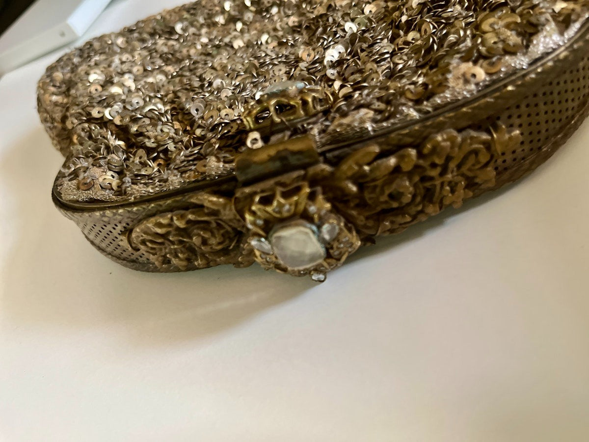Gold glittery clutch bag with intricate designs on a white surface