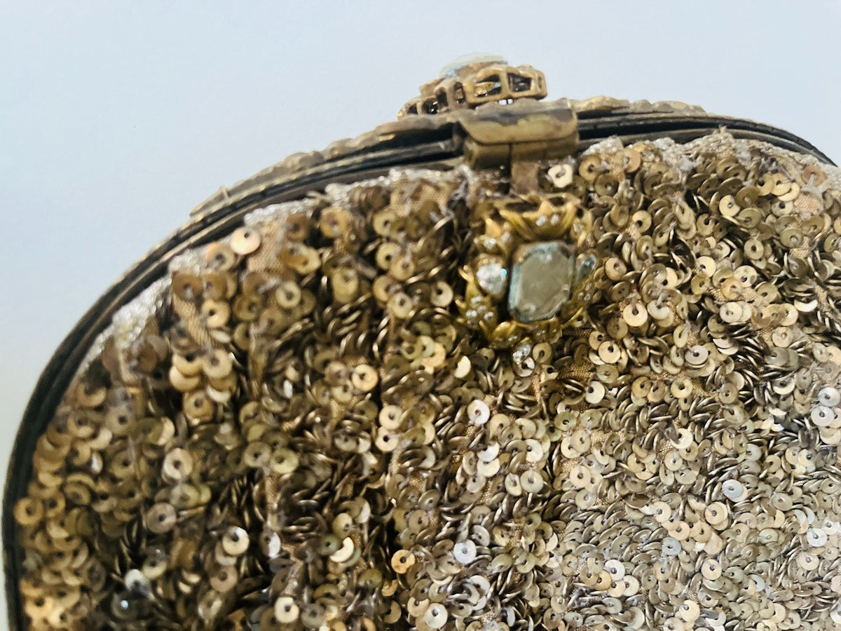Close-up of a gold sequin handbag with a decorative clasp on a light background