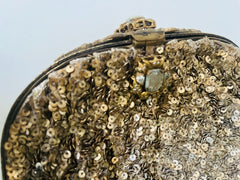 Close-up of a gold sequin handbag with a decorative clasp on a light background