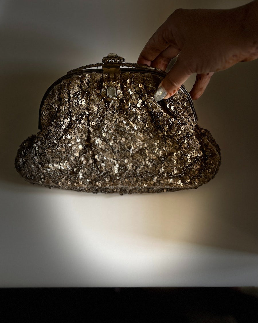 Hand holding a glittery handbag against a neutral background