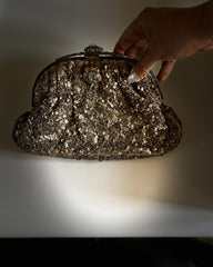 Hand holding a glittery handbag against a neutral background