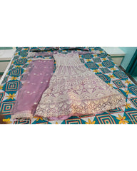 A lavender and white embroidered ethnic dress set laid flat on a patterned bedsheet, featuring a heavily embroidered white and lavender dress with matching sheer embroidered pants.