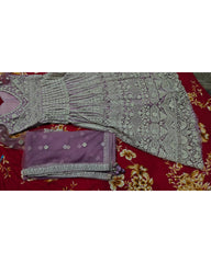 A flat-lay view of a traditional South Asian gown set, featuring a heavily embroidered lavender gown, a matching folded dupatta, and a red floral printed fabric underneath.
