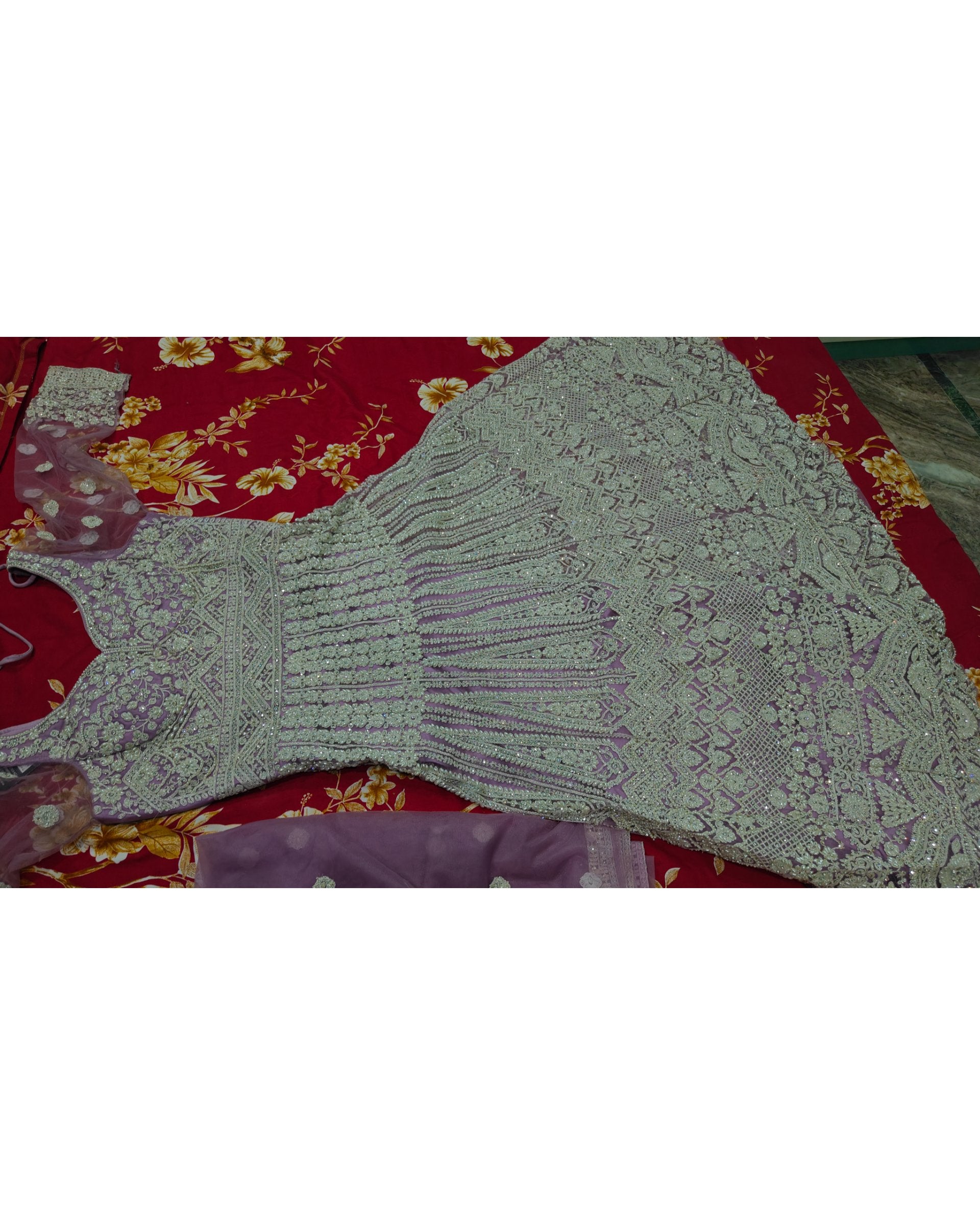 A light purple/lavender embroidered dress or kurta laid flat on a red floral fabric background.