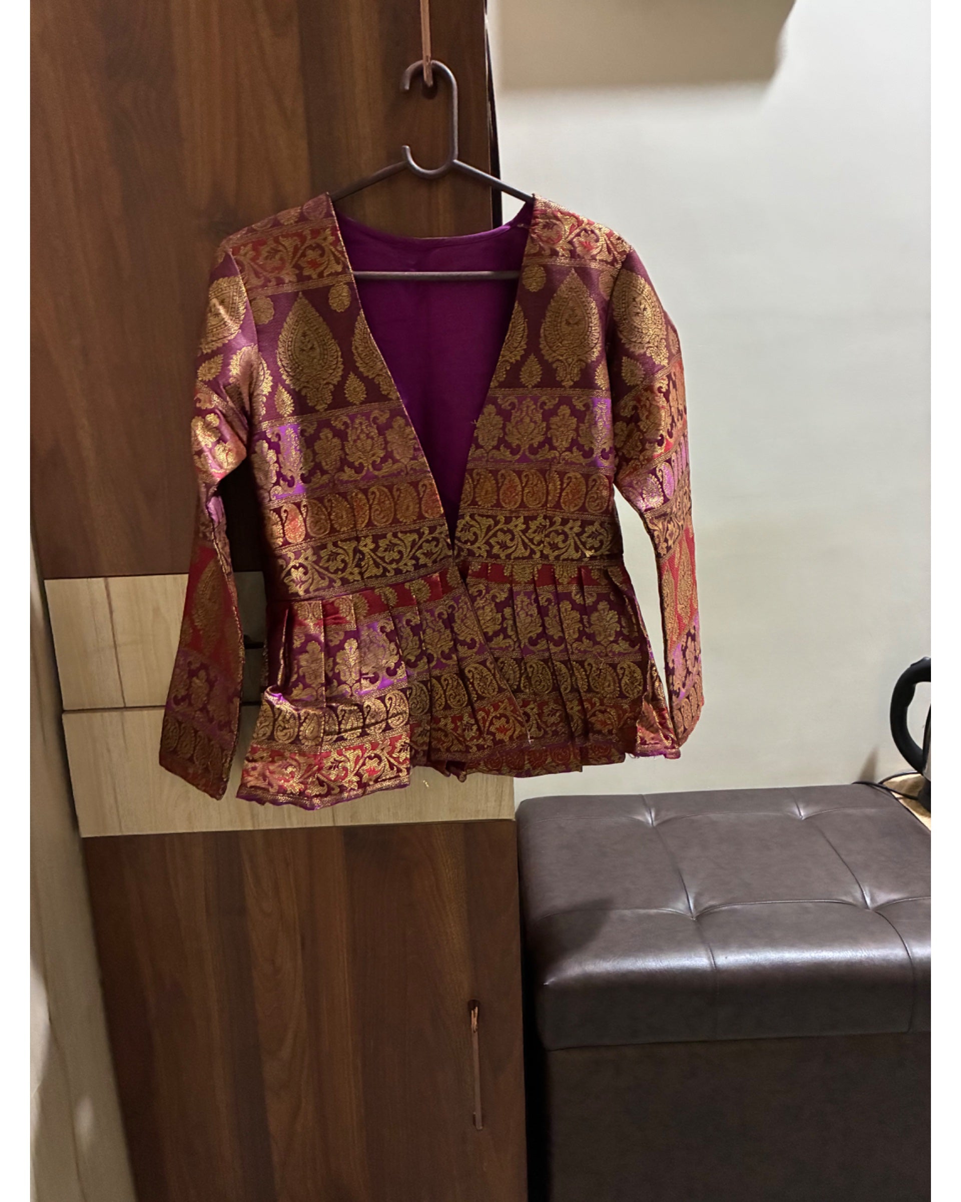 Brocade jacket on a hanger against a wooden wall.