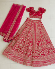 A traditional Indian lehenga choli set laid out on a light tiled floor. The set features a bright pink skirt heavily embroidered with gold and silver threadwork, a matching pink blouse with gold embroidery, and a coordinating pink dupatta with gold borders.
