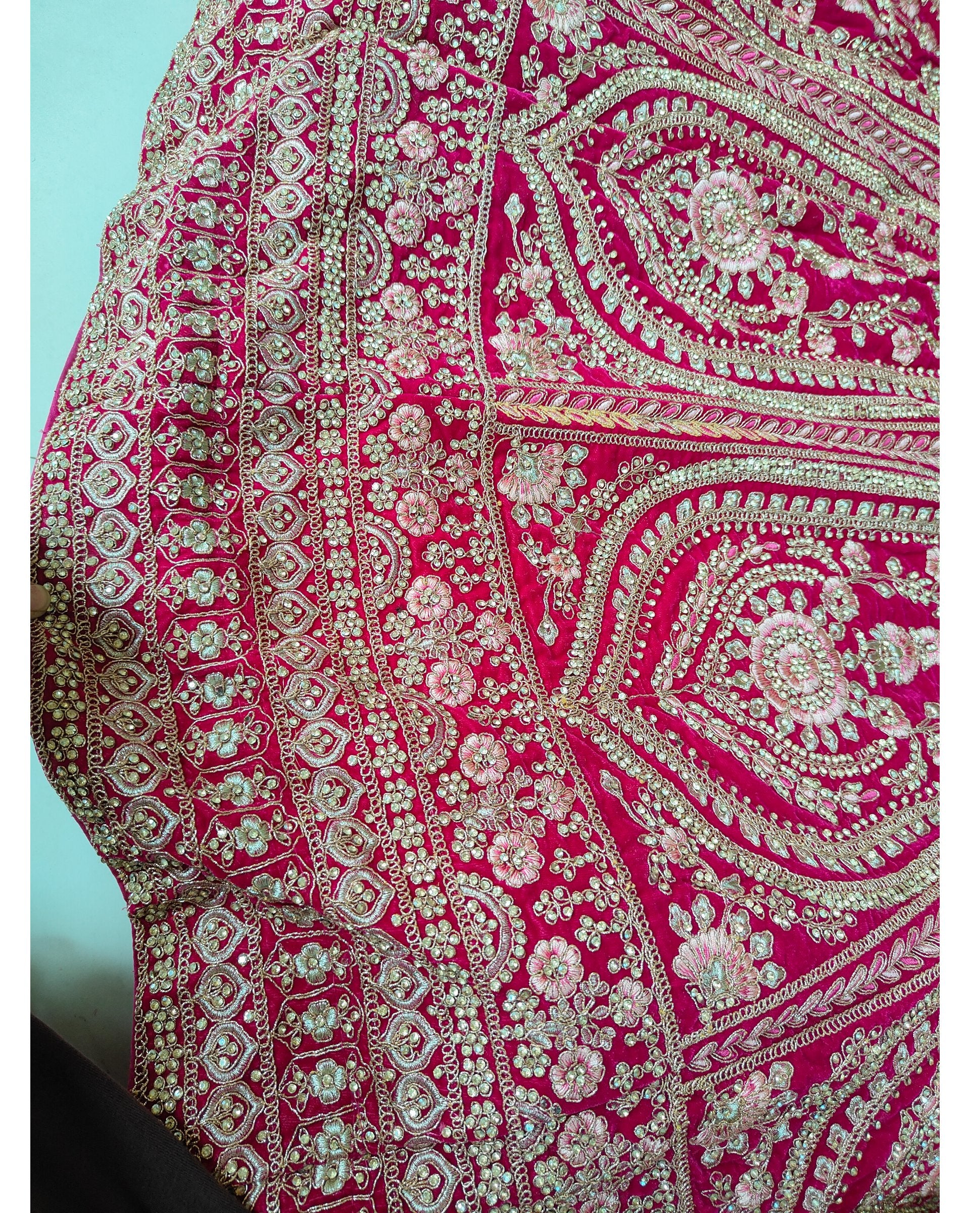 A close-up of a bright pink embroidered fabric with intricate metallic silver and gold floral, paisley, and geometric patterns.