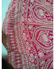 A close-up of a bright pink embroidered fabric with intricate metallic silver and gold floral, paisley, and geometric patterns.