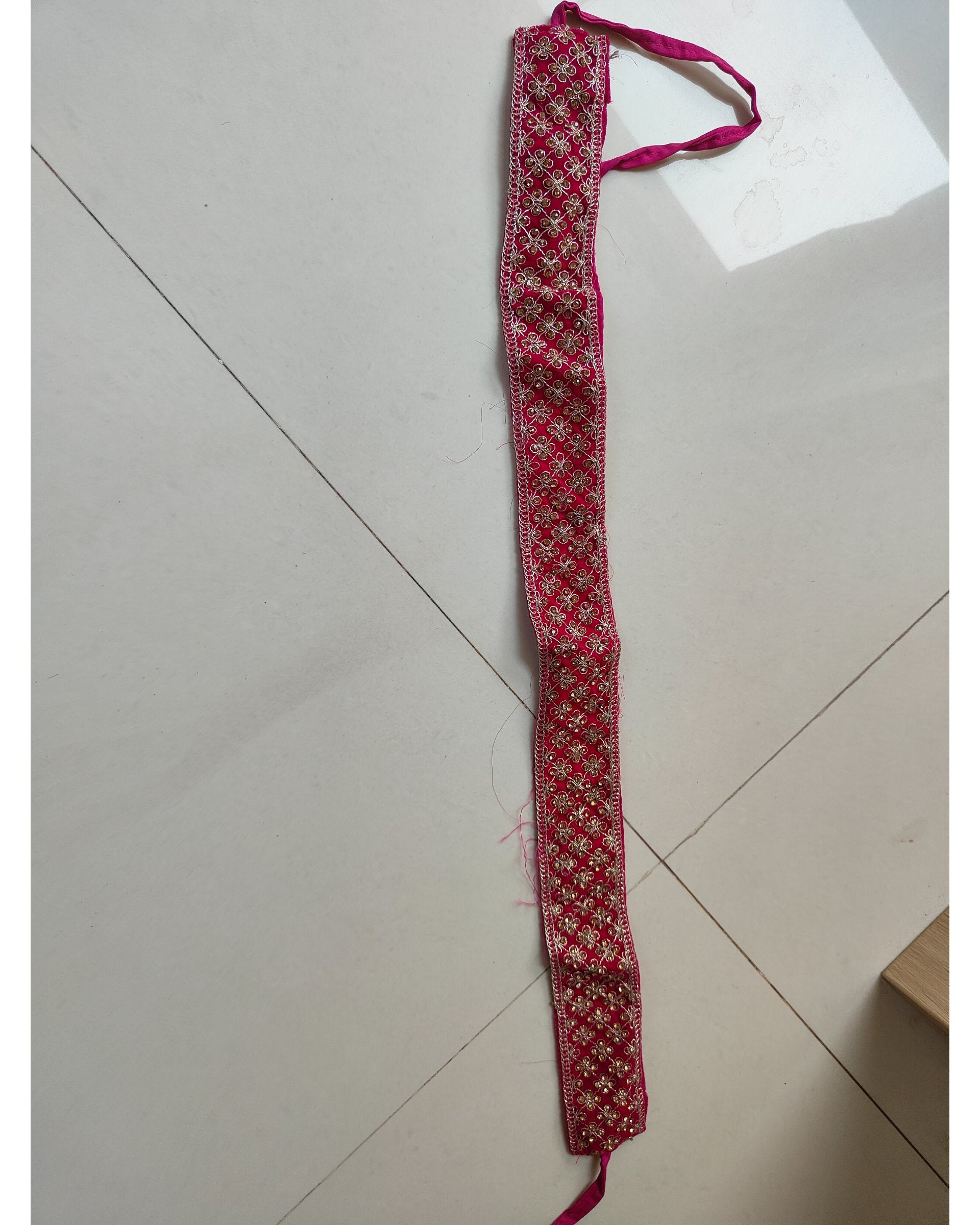 A long, narrow red and white patterned fabric belt or waist accessory with a matching red tie, laid out on a light beige tiled floor.