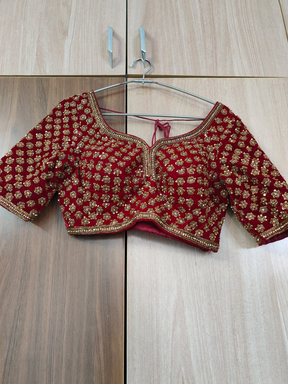 Red embroidered blouse on a hanger against a wooden floor background