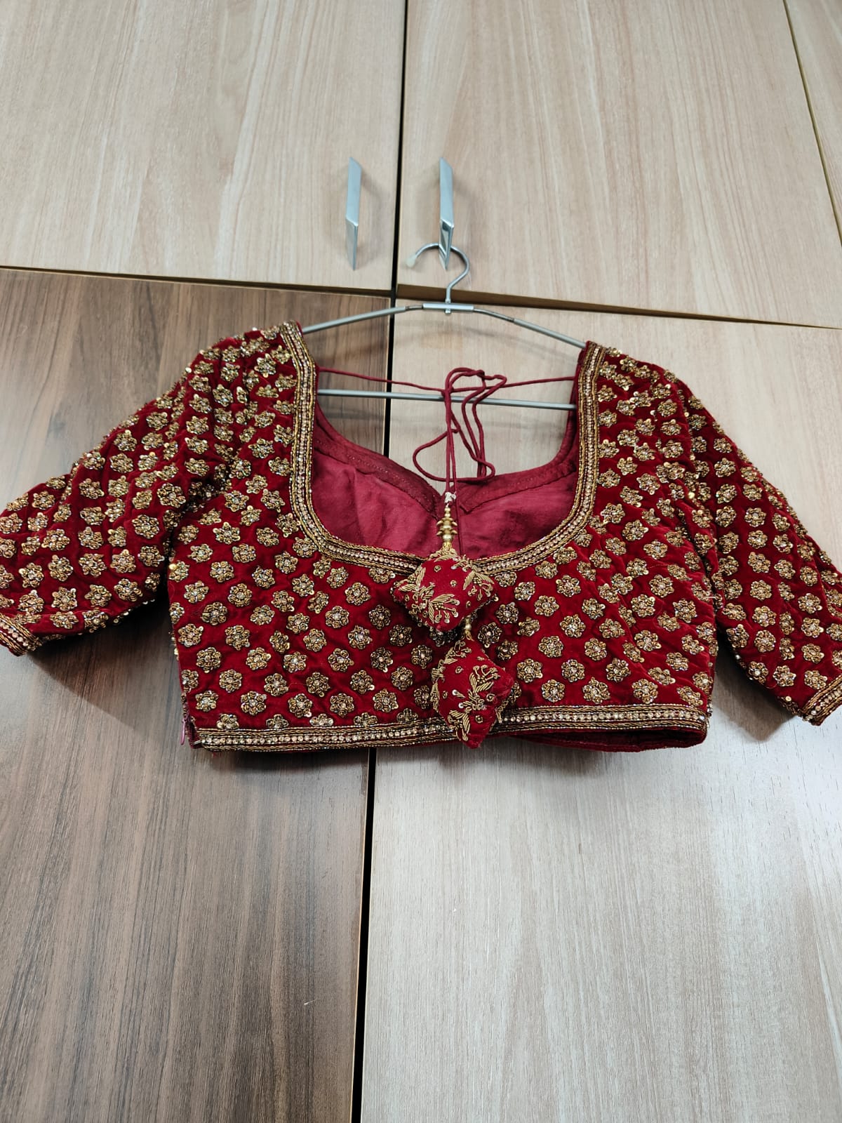 Back View of Red embroidered blouse on a hanger against a wooden floor background