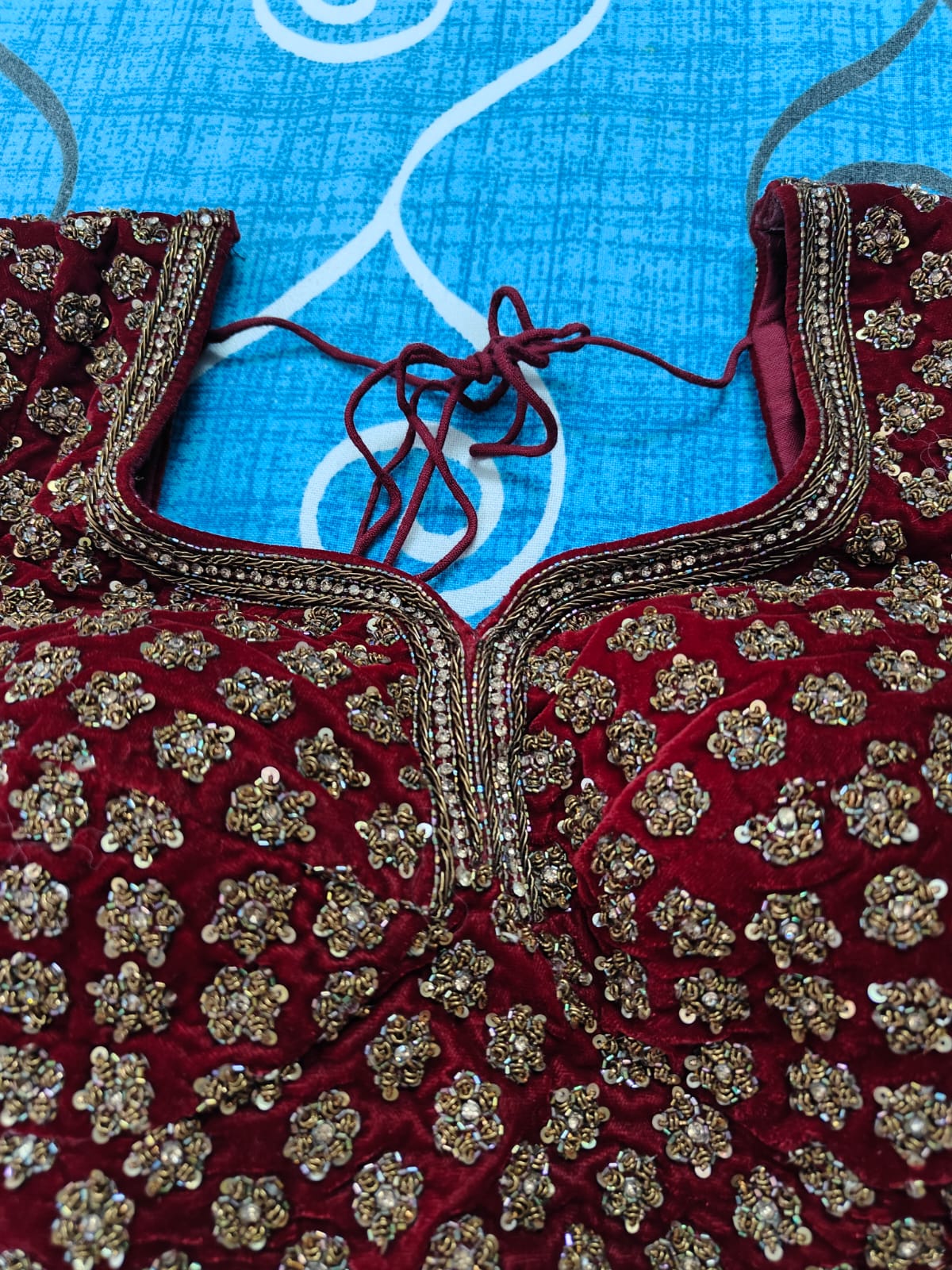 Maroon embroidered blouse with gold details on a blue fabric background
