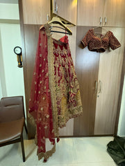 Red and gold embroidered traditional Indian bridal lehenga on a hanger against a wooden wardrobe.