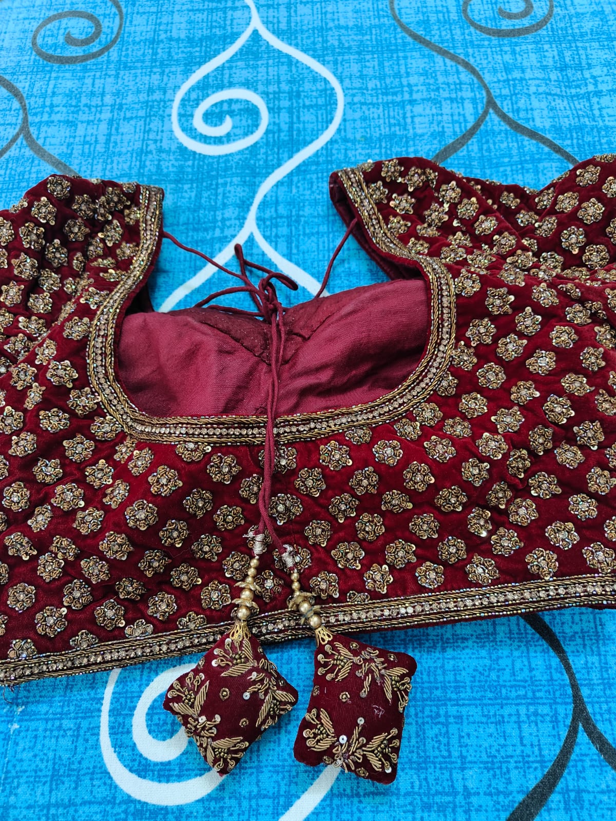 Back view of Maroon embroidered blouse with gold details on a blue fabric background