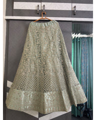 An olive green embroidered lehenga skirt with intricate metallic gold and silver floral patterns, hanging on a wooden hanger against a gray and white paneled wardrobe door.
