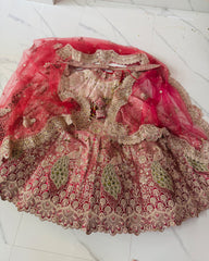 An ornate pink and gold embroidered bridal lehenga with a matching sheer pink dupatta, laid flat on a white marble tile floor.