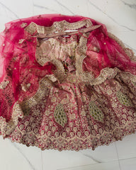 A heavily embroidered pink and beige traditional lehenga with a matching sheer pink dupatta, laid flat on a light marble surface. The fabric features intricate gold zari embroidery, sequins, and mirror work.